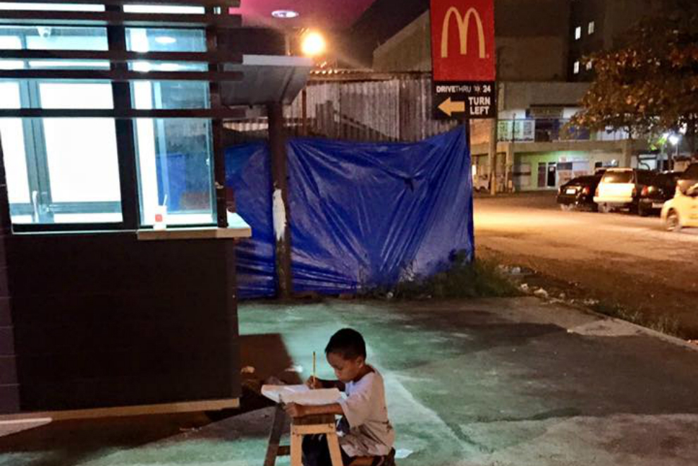 Straßenkind lernt nachts im Licht von McDonald’s